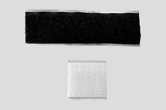 Ett svartvitt tygstycke med kardborrelås självhäftande fäst, och ett vitt tygstycke i en påse.